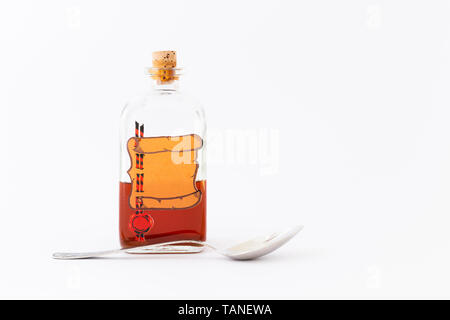 A vintage medicine bottle with cork filled with orange liquid and furnished with an empty label like a parchment roll with red sealing wax and a spoon