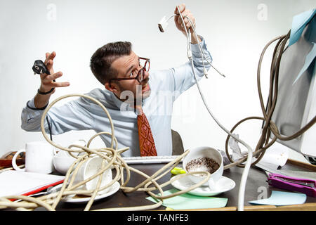 Completely confused. There are a lot of wires in the workplace and man is constantly tangled in them. It's literally blocking him. Concept of office w Stock Photo
