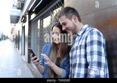 Happy couple talking about smart phone online content in the street of an old town Stock Photo