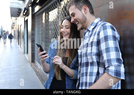 Funny couple checking smart phone online content standing in the street Stock Photo