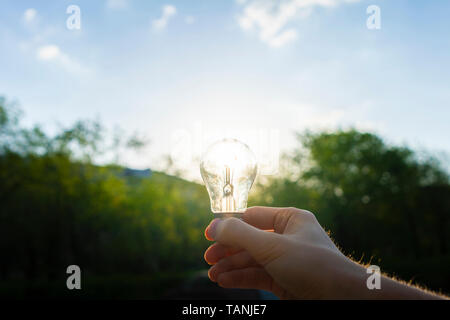 first person view of person hold light bulb outside at the nature, enegry concept with a sunshine through it Stock Photo