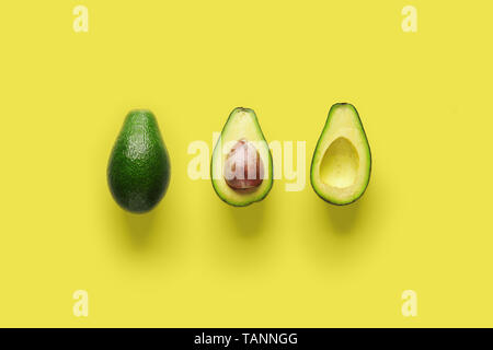 Whole avocado fruit and two halves in a row isolated on yellow background Stock Photo