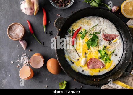 spicy scrambled eggs or omlette in a frying pan with bacon, garlic and pepper, ingredients around on the table