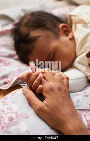 Close-up of loving black mother lying and holding small hand of sleepy baby while resting during daytime sleep of baby Stock Photo