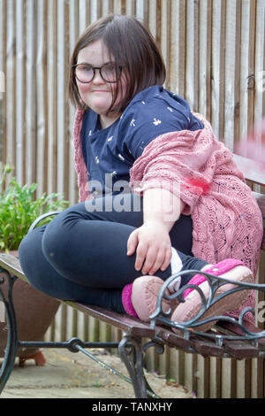 Girl with Downs Syndrome sitting on a garden bench enjoying life and the garden. Stock Photo
