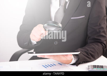 Businessman holding magnifying glass and digital tablet close up Stock Photo