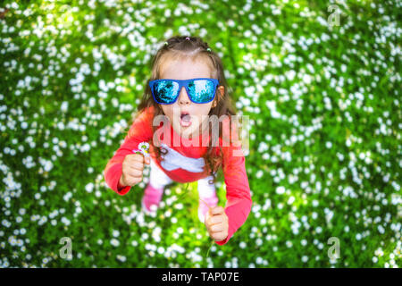 Happy smiling little girl with curly hair among the daisy field. Stock Photo
