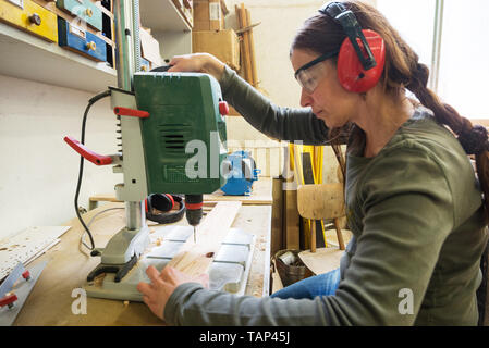 Young woman with drill perforating wood plank at workshop Stock Photo