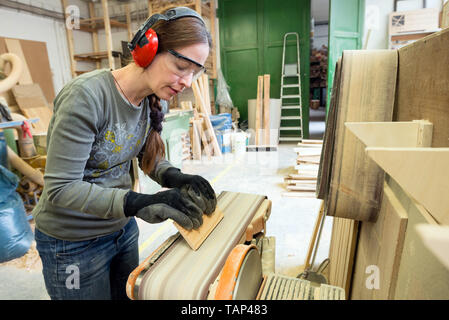 Young woman using a belt sander to sand wooden plank at workshop Stock Photo