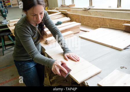 Young woman sanding wooden board using sand paper at workshop Stock Photo