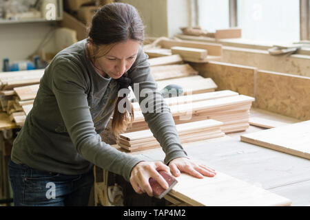 Young woman sanding wooden board using sand paper at workshop Stock Photo