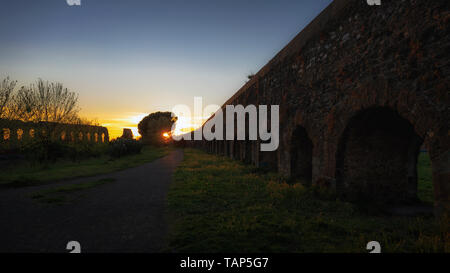 A country path in the center, and to the side the ruins of two ancient Roman aqueducts, photographed at sunset in the Aqueduct Park in Rome, Italy. Stock Photo