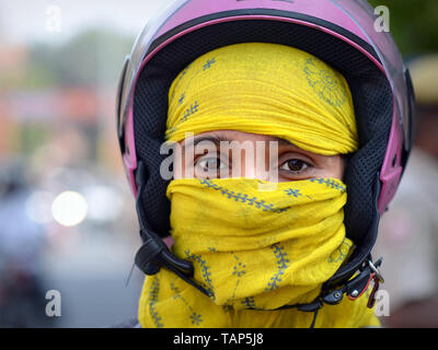 Indian Rajasthani scooter girl with a purple crash helmet covers her face with a yellow secular dust veil. Stock Photo