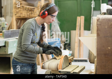 Young woman using a belt sander to sand wooden plank at workshop Stock Photo