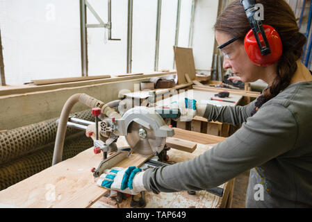 Young woman cutting a wooden plank with a circular saw in a workshop Stock Photo