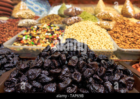 On the shelves of the eastern market are sold slides with prunes close-up, against the background of various nuts in a blurred form. Stock Photo
