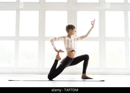 Young attractive woman practicing yoga, standing in Horse rider exercise, anjaneyasana pose, working out, wearing sportswear, cool urban style Stock Photo