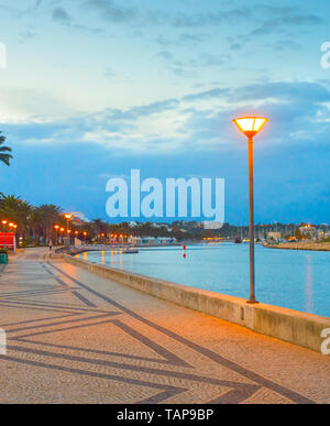 Lagos embankment evening scene with glowing street lanterns and palm alley, Portugal Stock Photo