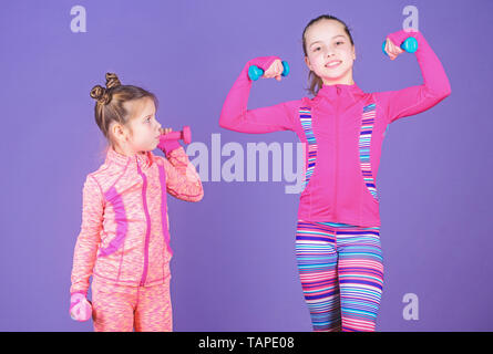 Motivation and sport example concept. Toddler repeat exercise after sister. Sport exercises for kids. Healthy upbringing. Sporty babies. Following her sister. Girls cute kid exercising with dumbbells. Stock Photo