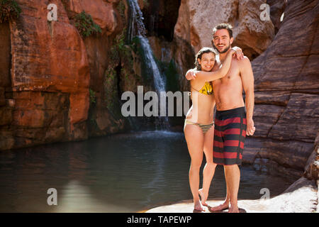 Portrait of a smiling young couple standing near a waterfall. Stock Photo