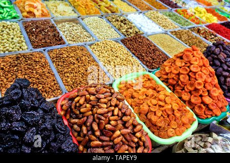 On the shelves of the eastern market are sold slides with dates close-up, dried apricots, prunes against the background of various nuts in a blurred f Stock Photo