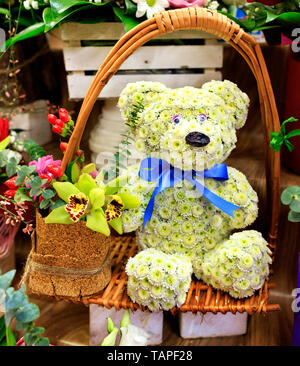 Close-up of a beautiful composition of a toy bear from small blooming chrysanthemums in a wicker basket frame with a large orchid flower. Stock Photo