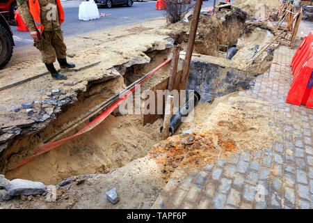 A road service worker stands near an excavated trench on the roadway and inspects concrete blocks, wells, city sewer pipes and paving slabs. Stock Photo