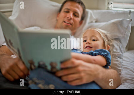 Father lying down reading a book with his daughter. Stock Photo