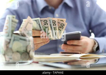 Male hand holding pack of banknotes and cellphone making some calculation planning his future expenses closeup Stock Photo