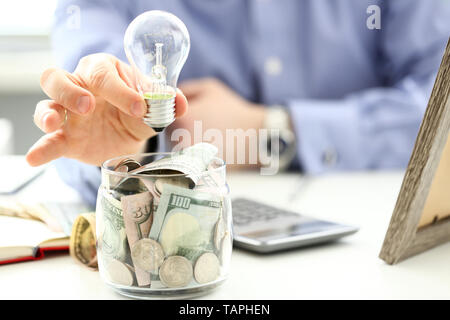 Male arm holding lightbulb over tip can full of US money Stock Photo