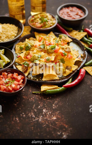 Fresh yellow corn nacho chips garnished with melted cheese, peppers and tomatoes in a handmade ceramic plate on rusty table Stock Photo