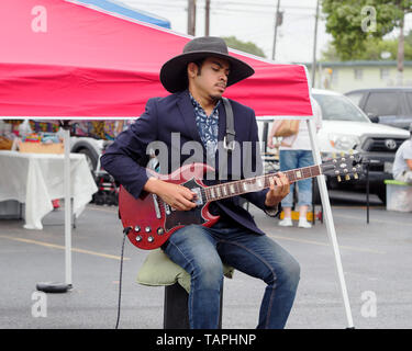 A handsome young man with dark complexion in a black, wide-brimmed hat plays an electric guitar at the Corpus Christi Southside Farmers' Market. Stock Photo