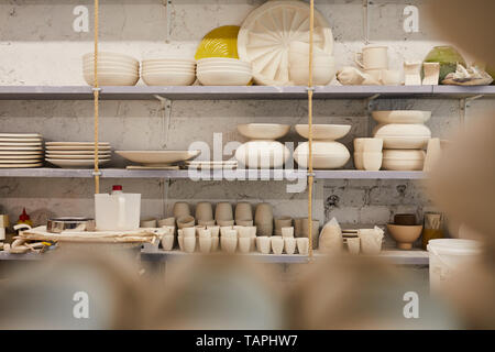 Beautiful creative ceramic dishware of different shapes placed on shelves in store or pottery workshop, copy space Stock Photo