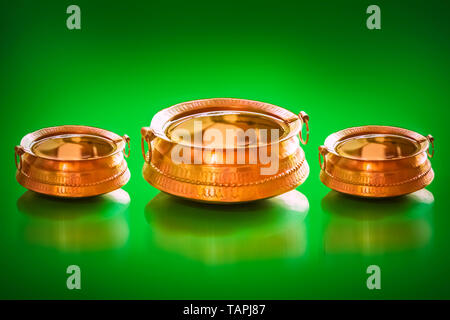 Traditional Brass Pot with full of water and coins inside for lucky charm decorative handles and legs isolated on a green background. Stock Photo