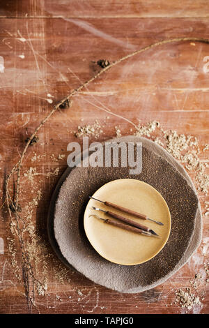 High angle view of craft knives and cutters on stacking ceramic plates place on scratched table with sawdust Stock Photo