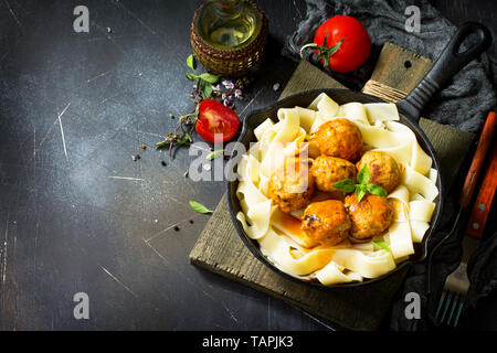 Fettuccine pasta and Homemade Beef meatballs in tomato sauce in a frying pan on dark stone table. Free space for your text. Stock Photo