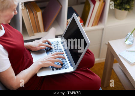 Contemporary mobile woman with laptop on her knees typing on keypad and looking for online websites or information Stock Photo