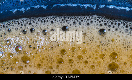 Foam surface texture. Bubble drink detail. Aromatic hot coffee cup. Refreshing caffeine beverage in blue glass. Water drop. Abstract frothy background. Stock Photo