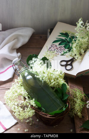 Homemade syrup of elderberry flowers in a glass jar and elder branches on a wooden table Rustic style. Stock Photo