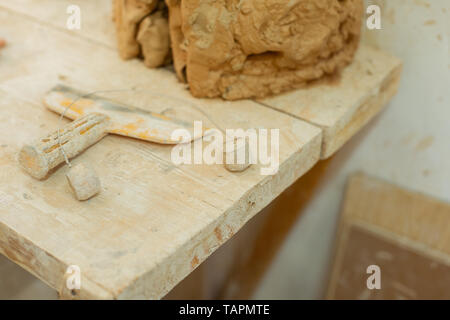 Fresh unprocessed clay. Dirty metal tool lying on a wooden table covered in clay layer during intense working day Stock Photo