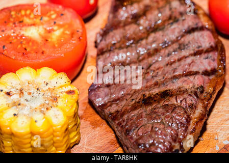 Close up freshly grilled steak on wood with tomatoes and corn Stock Photo