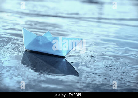 Lonely blue paper boat in shallow water. Blue toned image. Stock Photo