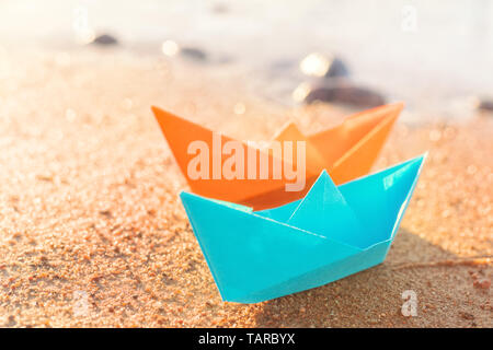 Orange and blue paper boats, blue and orange, on sandy beach outdoors. Selective focus on front Stock Photo