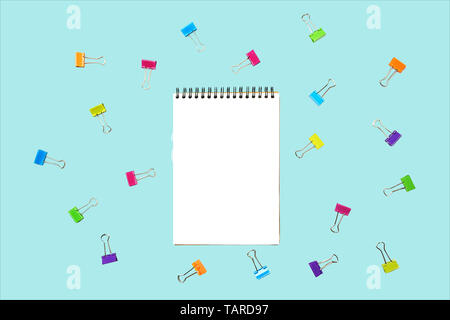 Back to school background with notepad, colorful paper clips on pastel blue backdrop. Stock Photo