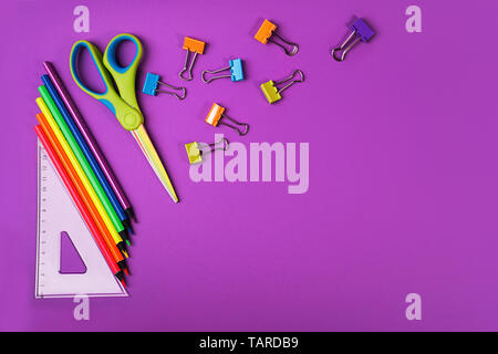 Back to school background with pencils, square ruler, scissors, paper clips on purple backdrop. Stock Photo