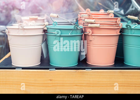 Various multicolored bright small ornamental metal buckets for sale on wooden table outdoors. Many colorful decorative mini pails for garden flower Stock Photo