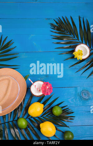 Tropical summer background with hat, palm leaves, lemons, lime, coconuts on blue wooden background Stock Photo