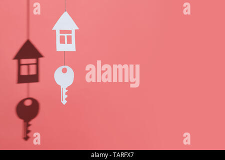 a small house and key made of cardboard casts a shadow on a bright colored background Stock Photo
