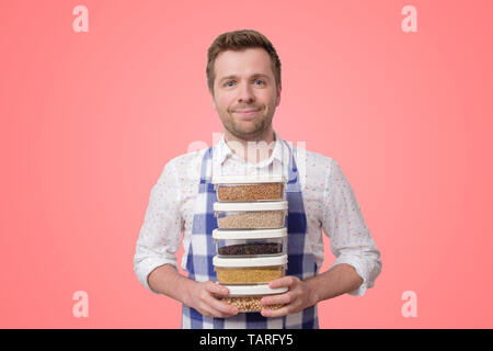 Young smiling man in apron hold several boxes with cereals Stock Photo