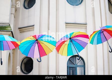 Colored bright rainbow umbrellas on the light old wall background Stock Photo